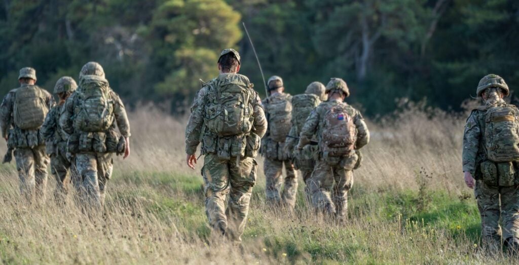 8 British army soldiers tabbing with 25Kg bergens across open countryside